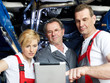 Three mechanics inspecting the engine of a car with touchpad