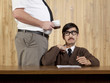 Boss by stressed businessman at desk in office
