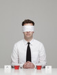 Studio portrait of young man with blindfold sitting in front of two glasses with red liquid