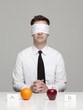 Studio portrait of young man with blindfold choosing between orange and apple