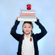 Studio shot of girl (10-11) holding stack of books and apple on head