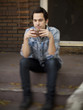 "USA, Utah, Provo, Young man with mug sitting on steps in front of house"