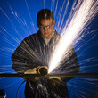 man in blue coveralls with a power grinder