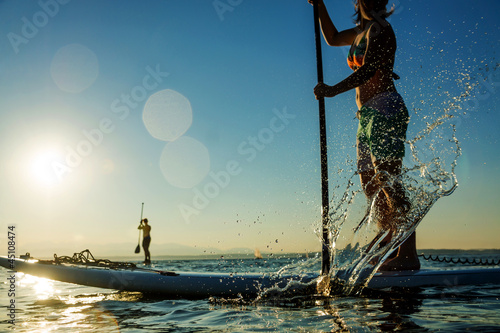 Photo: Women on Stand Up Paddle Board with Water Splash Women on Stand Up Paddle Board with Water Splash