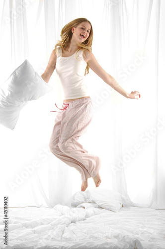 Photo: blond woman holding pillow jumping on her bed blond woman holding pillow jumping on her bed