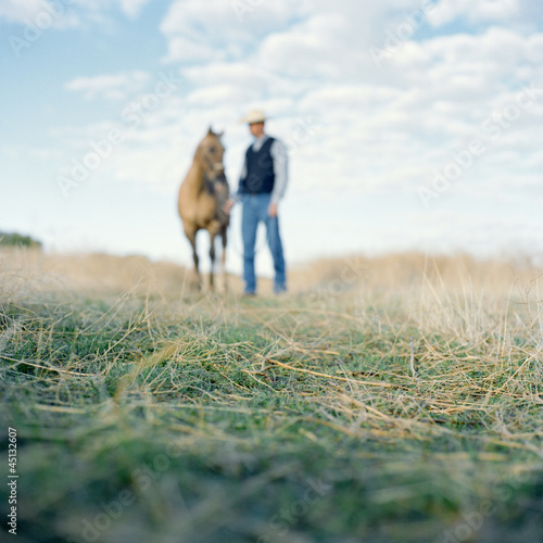 Photo: "USA, Utah, Mapleton, Cowboy standing with horse at pasture, focus on grass" "USA, Utah, Mapleton, Cowboy standing with horse at pasture, focus on grass"