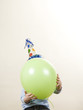 child wearing a party hat holding a balloon in front of his face