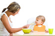 young mom spoon feeding her cute baby girl isolated on white