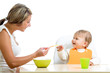 young mother spoon feeding her cute baby girl isolated on white