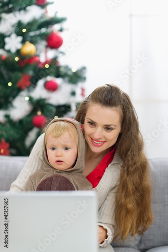 Photo: Mother and baby near Christmas tree using laptop Mother and baby near Christmas tree using laptop