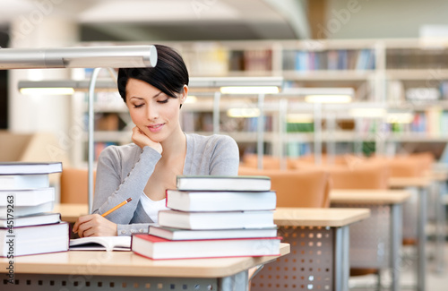 Photo: Beautiful student studies with piles of books Beautiful student studies with piles of books