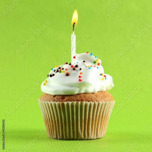 Photo: tasty birthday cupcake with candle, on green background tasty birthday cupcake with candle, on green background
