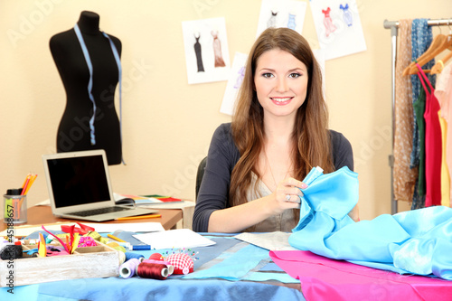 Photo: beautiful young dressmaker in workroom beautiful young dressmaker in workroom