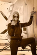 Beautiful girl in jacket standing next to war aircraft.