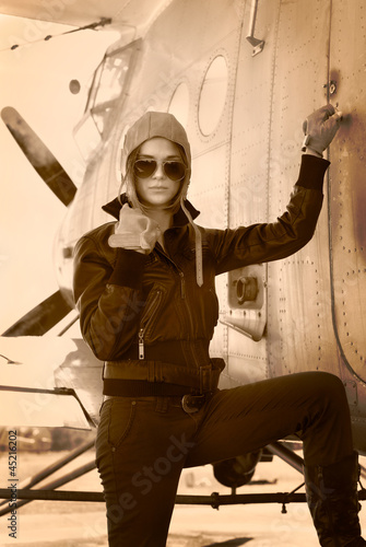 Photo: Beautiful girl in jacket standing next to war aircraft. Beautiful girl in jacket standing next to war aircraft.