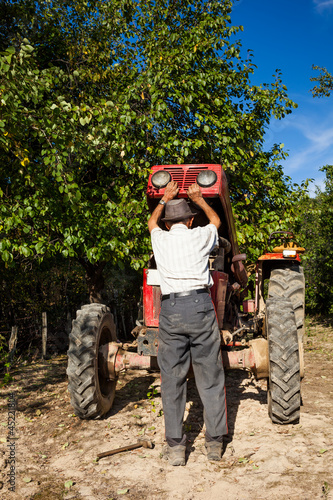 Photo: Senior farmer repairing his tractor Senior farmer repairing his tractor