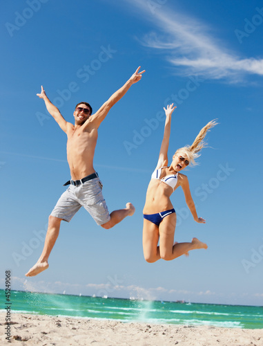Photo: happy couple jumping on the beach happy couple jumping on the beach