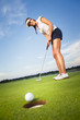 Happy girl golfer putting ball into hole.