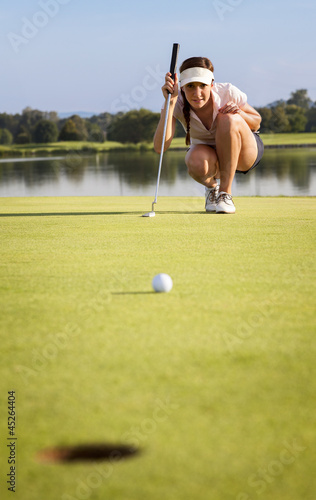 Photo: Girl golfer analyzing the green for putting the ball into cup. Girl golfer analyzing the green for putting the ball into cup.