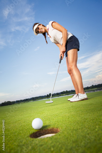 Photo: Happy girl golfer putting ball into hole. Happy girl golfer putting ball into hole.