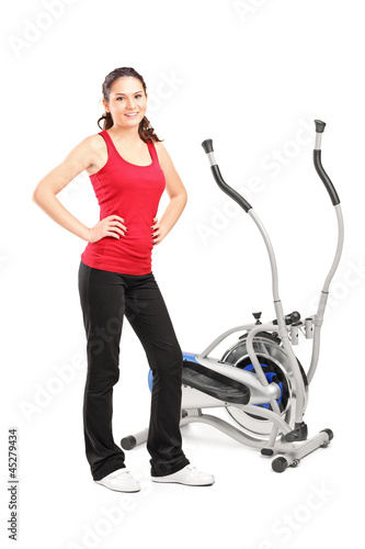 Photo: Young female posing next to a cross trainer Young female posing next to a cross trainer