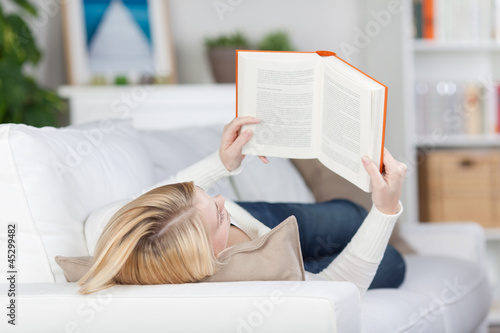 Photo: blonde frau liest ein buch auf dem sofa blonde frau liest ein buch auf dem sofa
