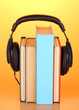Headphones on books on wooden table on orange background