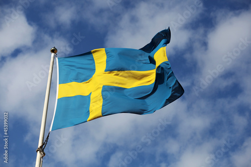 Photo: Waving swedish flag against blue sky with small white clouds Waving swedish flag against blue sky with small white clouds