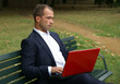 Businessman with a red laptop, sitting on a bench