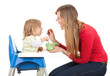 young mother feeding hungry baby in highchair