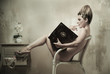 Naked woman sitting in a chair reading a book indoors