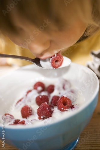 Photo: Small child eating yoghurt with fresh raspberries Small child eating yoghurt with fresh raspberries