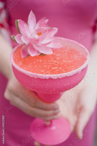 Photo: Woman holding a cocktail in a pink glass decorated with a flower Woman holding a cocktail in a pink glass decorated with a flower