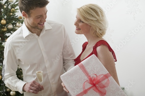 Photo: Woman holding large Christmas parcel, man holding glass of wine Woman holding large Christmas parcel, man holding glass of wine
