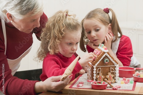 Photo: Small girls and grandmother decorating gingerbread house Small girls and grandmother decorating gingerbread house