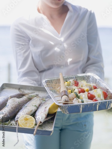 Photo: Woman holding trays of fish & kebabs ready for grilling, outdoors Woman holding trays of fish & kebabs ready for grilling, outdoors