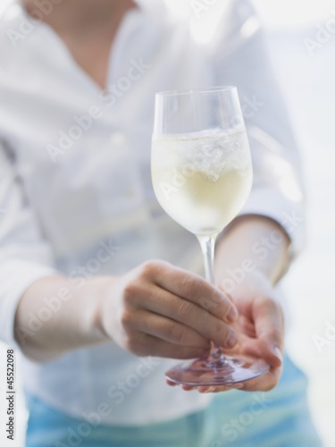 Photo: Woman holding glass of white wine with ice cubes out of doors Woman holding glass of white wine with ice cubes out of doors