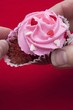 Taking chocolate cupcake with pink icing out of paper case