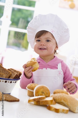 Photo: Little girl in chef's hat sitting at table with muffins Little girl in chef's hat sitting at table with muffins