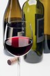 A glass of red wine and a cork in front of wine bottles