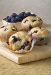 Four Blueberry Muffins on a Cutting Board with Fresh Blueberries; On Bitten
