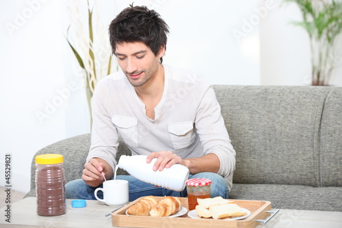Photo: Young man having breakfast in his living room Young man having breakfast in his living room