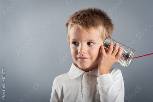 Photo: Young boy listen to tin can telephone. Young boy listen to tin can telephone.