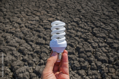 Photo: energy saving lamp in hand over drought earth energy saving lamp in hand over drought earth