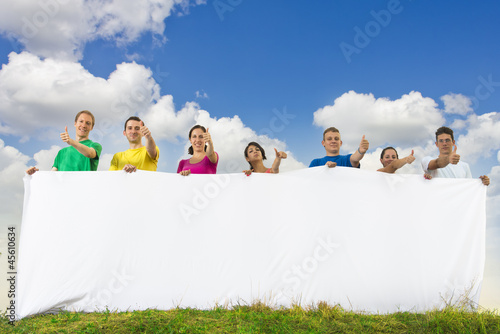 Photo: Group of young people holding a big blank paper in nature Group of young people holding a big blank paper in nature