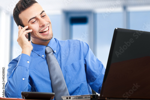 Photo: Businessman sitting at the desk and talking at the phone Businessman sitting at the desk and talking at the phone