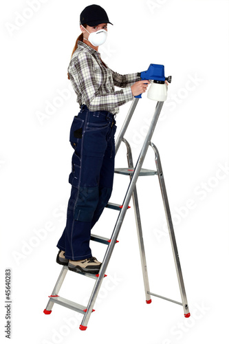 Photo: A female painter with a spray gun on a ladder. A female painter with a spray gun on a ladder.