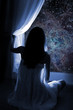 Foto: Young girl standing by the window, watching the stars Young girl standing by the window, watching the stars