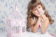 Tender dreamy romantic girl with wavy hair near open birdcage