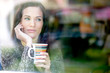 Winter portrait of a young woman looking out the window enjoying